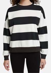 Femme portant un pull à manches longues rayé horizontalement noir et blanc, avec des poignets et un ourlet noirs, associé à un pantalon noir.