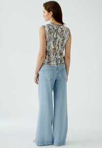 Ärmelloses Top mit Schlangenprint-Muster in Beige-, Grau- und Brauntönen. Kombiniert mit hochtaillierten, weit geschnittenen hellblauen Jeans.