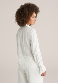Camicia bianca con un motivo testurizzato e morbidi polsini a volant. Presenta un colletto classico e una vestibilità morbida con un tessuto leggero.