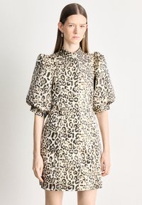 Krótka sukienka w cętki lamparta z bufkami na rękawach, wysokim kołnierzem i detalami z guzikami. Wykonana z lekkiego materiału o gładkiej teksturze.