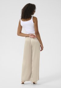Pantalons larges beiges en tissu lisse, avec une taille élastique. Portés avec un débardeur blanc au design simple.
