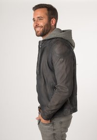 Giubbotto in pelle grigio scuro con finitura testurizzata, dotato di cappuccio grigio, tasche con zip e design aderente.