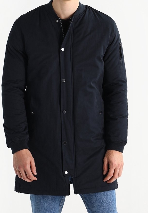 Giacca bomber blu navy con zip frontal, bottoni a pressione e tasche laterali. Presenta un colletto a coste e una tasca con zip sulla manica sinistra.