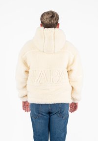 Crèmekleurige pluchen hoodie van gestructureerde stof, met een verdiept "NAPA" logo op de achterkant, oversized pasvorm en een capuchon.