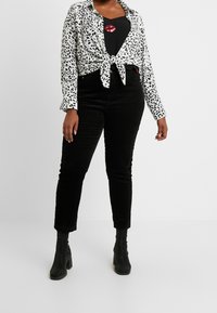 Hvid skjorte med sort leopardprint, knyttet i taljen, over en sort tanktop med læbe-grafik. Sorte corduroy bukser og sorte hælede støvler.