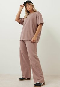 Dammig rosa bomulls-t-shirt med nedsläppta axlar, parat med matchande löst sittande byxor. Svart keps och svarta sneakers med vita ränder.