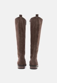 Egy pár magas barna velúrbakancs, amely függőlegesen áll, hátulról látható, alacsony fából készült sarkakkal és felhúzó fülekkel a tetején.