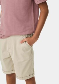 Avslappnad kortärmad skjorta i ljusrosa med vertikala ränder, tillsammans med beige shorts med sidan fickor och uppvikta ben.