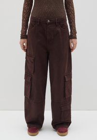 Braune Cargo-Hosen mit mehreren Taschen, lockere Passform und glatter Textur, kombiniert mit roten Schuhen mit strukturiertem Boden.