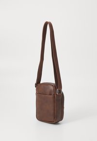 Brown leather crossbody bag with a rectangular shape, zip closure, adjustable strap, and front pocket detail. Smooth texture.