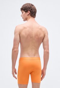 Oranžové boxerky s hladkou textúrou a elastickým pásom, zobrazené zozadu, zdôrazňujúce strih a dizajn.