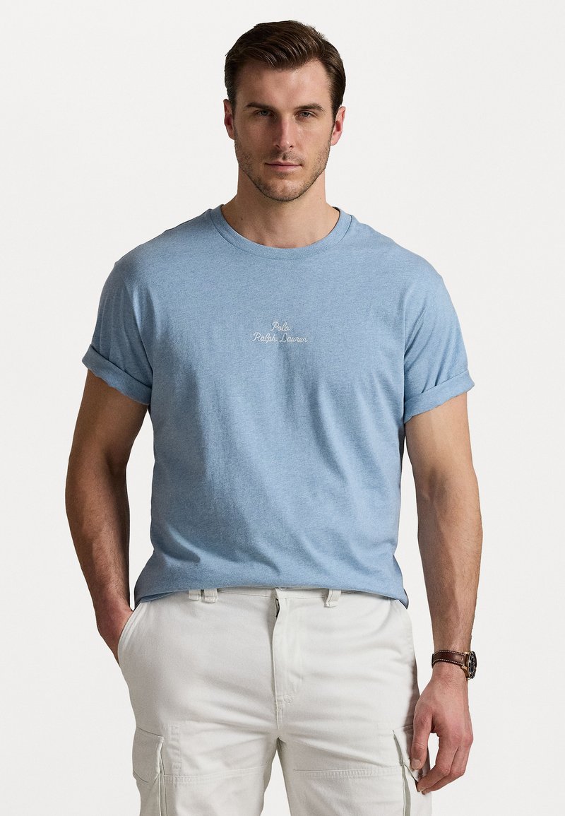 Gaiši zils īsām piedurknēm t-krekls ar sarullētām piedurknēm, uz kura krūtīm ir izšūts "Polo Ralph Lauren" logo, izgatavots no mīkstas kokvilnas auduma.