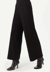 Svarta vida byxor i mjukt tyg med elastisk midja, som har sidofickor och en slät yta.