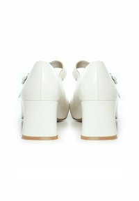 Zapatos de tacón alto blancos con punta redonda y correa en el tobillo, con un material de piel suave y un diseño de tacón grueso.