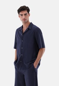 Marineblaues kurzärmliges Hemd mit Knöpfen aus strukturiertem Stoff, entspanntem Kragen und halber Knopfleiste, kombiniert mit passenden Shorts.