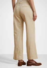 Pantaloni beige cu picioare largi, realizati dintr-un material moale, cu buzunare la spate și o croială lejeră, asortați cu mocasini maro.