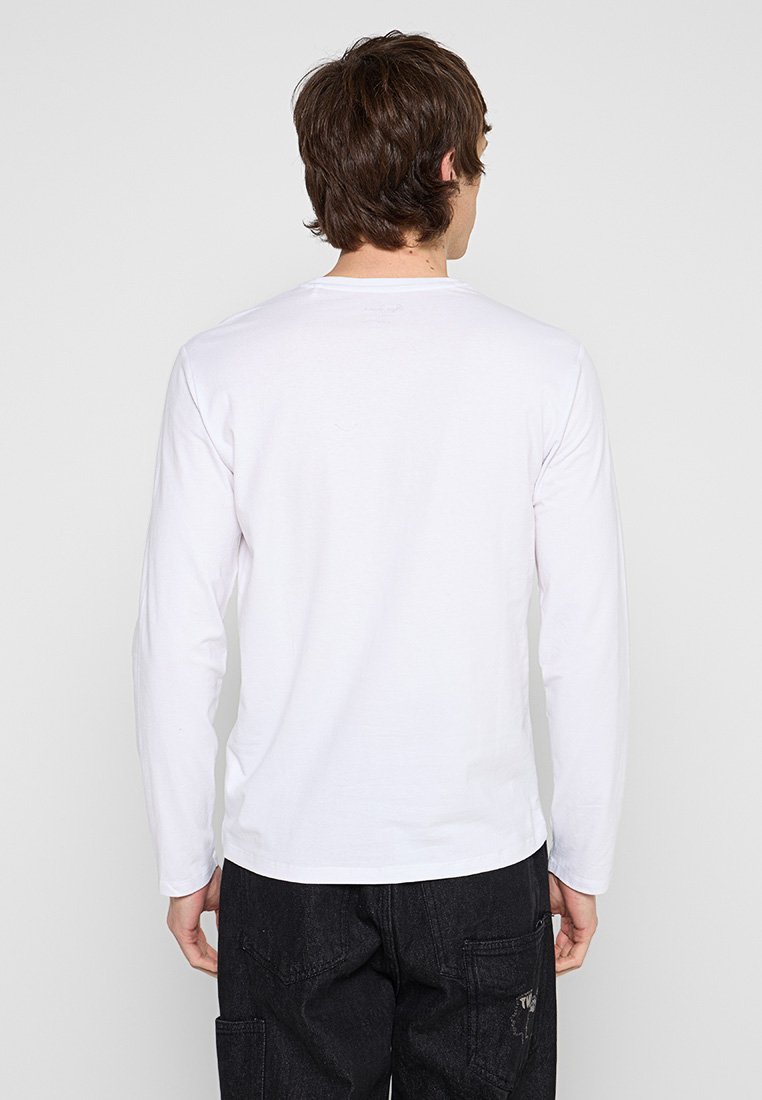 Camiseta blanca de algodón de manga larga con cuello redondo, textura suave y espalda lisa, combinada con pantalones cargo negros con bolsillos.