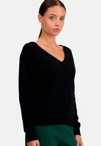 Pull noir en V avec des manches longues et une texture douce. La coupe est décontractée, fabriquée en tricot léger.