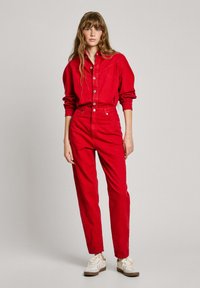 Combinación de camisa y pantalones de mezclilla rojos, con cierre frontal de botones, mangas largas y ajuste de tiro alto. Zapatillas blancas con detalles en marrón.