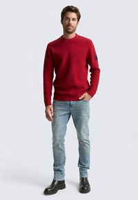 Maglione rosso con motivo a maglia strutturata, collo rotondo e polsini a coste. Abbinato a jeans azzurri e stivali in pelle nera.