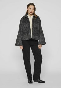Pelēks apgrieztais žakets ar faktūru, platām piedurknēm un divām priekšējām kabatām, kopā ar krēma krāsas džemperi un melnajām biksēm.