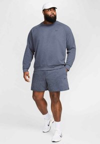 Sudadera atlética azul oscuro de manga larga y pantalones cortos a juego, ambos fabricados con tela suave. Una gorra blanca y zapatillas completan el conjunto.