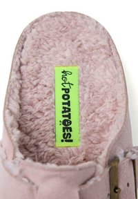 Zapatilla de casa de color rosa claro, suave y esponjosa, con forro blando, que cuenta con una etiqueta verde que dice "¡patatas calientes!" y una correa trasera beige con detalles metálicos.