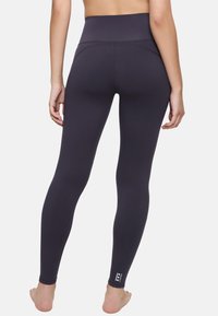 Leggings noirs taille haute au design ajusté et élégant, fabriqués en tissu extensible. Présentent un logo subtil au niveau de la cheville et aucune couture visible.