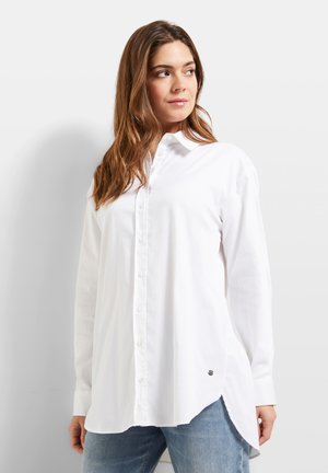 White cotton button-up shirt with long sleeves, a pointed collar, and a side slit. Features a small metal logo accent near the hem.