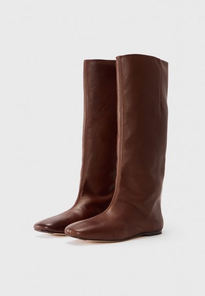 Bottes en cuir marron jusqu'aux genoux avec un design élégant, des bouts pointus et des coutures minimales. Texture lisse avec une finition légèrement brillante.
