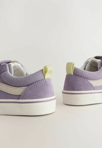 Paarse suede sneakers met een crème zijstreep, witte zool en contrasterende lichtgroene hielkap. Textuur bovenwerk en minimalistisch ontwerp.
