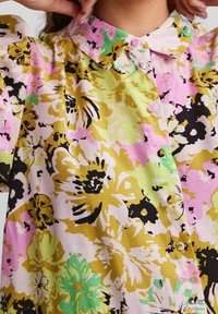 Bloemige blouse in een mix van roze, geel, groen en zwart; heeft een kraag, knoopsluiting en een textiel met een zachte, losse pasvorm.
