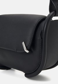 Borsa a spalla in pelle nera con una texture liscia, forma curva e accenti in metallo argentato. Presenta cuciture dettagliate e una chiusura a coperchio.