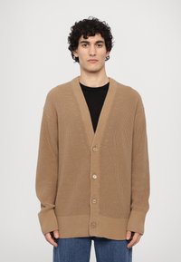 Beige strikket cardigan med V-hals, ribbede mansjetter og fem knapper, med et teksturert mønster gjennom hele stoffet. Casuall passform.