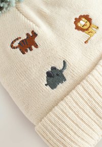 Crèmekleurige gebreide stof met een geborduurde tijger, leeuw en olifant in cartoonstijl nabij een geribbelde manchette.