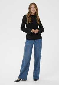 Sort blonde langærmet top med flæseærmer, parret med vide blå denim jeans og sorte hælede mules. Minimalistisk design, struktureret stof.