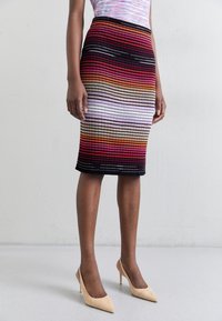 Strickrock mit einem Farbverlauf von Rot, Orange, Pink und Schwarz, mit gerippter Textur und einer figurnahen Silhouette.