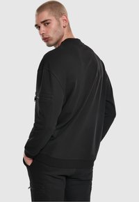 Felpa nera in tessuto liscio, con vestibilità comoda, scollo rotondo e tasca con zip sulla manica sinistra.