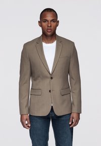 Beżowa marynarka o dopasowanym kroju, z dwoma przednimi kieszeniami i trzema guzikami. Noszona na białej koszuli i zestawiona z ciemnoniebieskimi dżinsami.