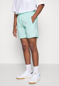 Mintgrønne shorts med elastisk talje og sidelommer samt hvidt logo; parret med hvide sneakers og ankelsokker.