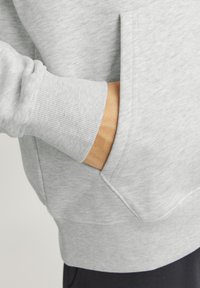 Szary sweatshirt z prążkowanym mankietem i kieszenią. Materiał ma gładką fakturę z subtelnym wzorem. Detale obejmują przeszycie przy krawędzi kieszeni.