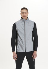 Grau ärmellose Jacke mit hohem Kragen, schwarzem Stoff an den Seiten und Ärmeln, mit einem Reißverschluss vorne und Logo auf der Brust.