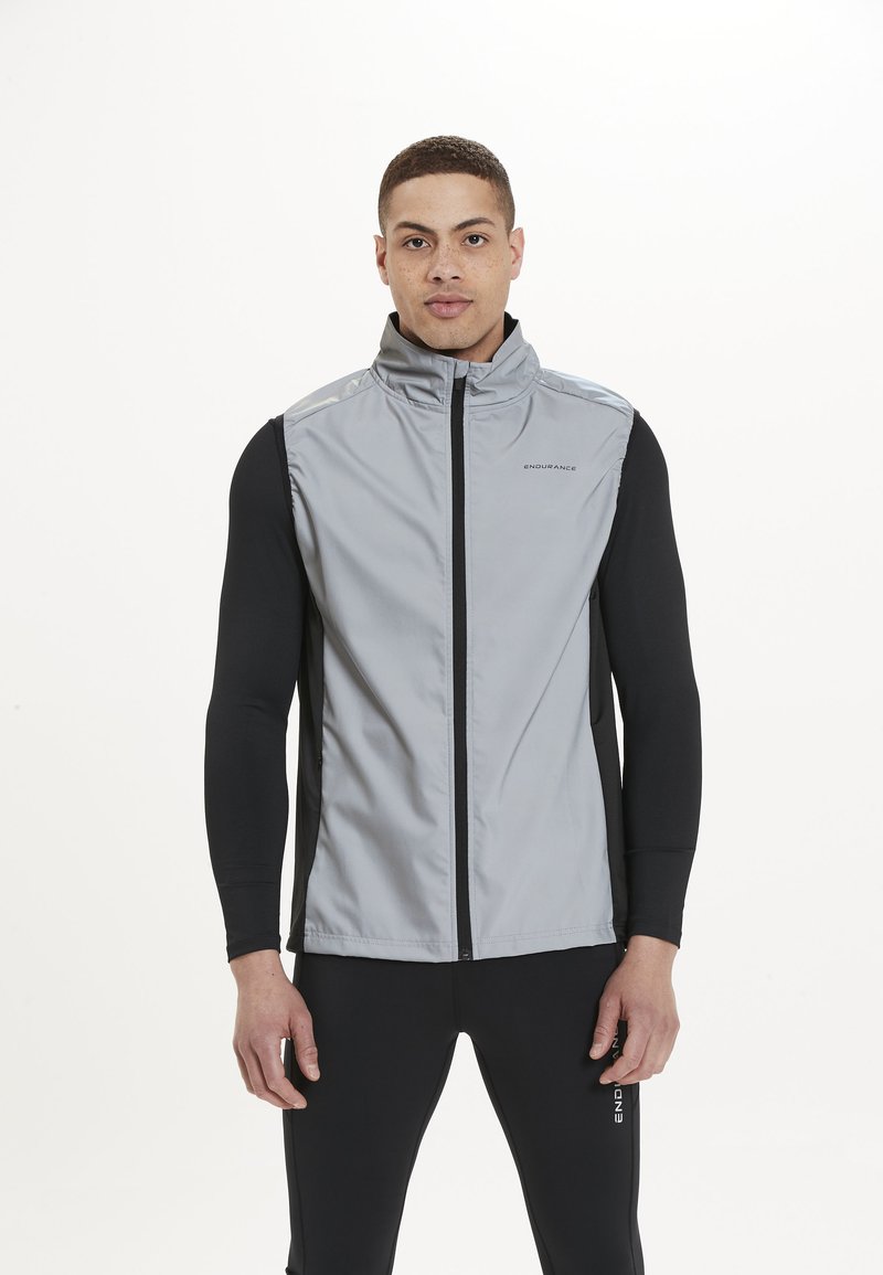 Grau ärmellose Jacke mit hohem Kragen, schwarzem Stoff an den Seiten und Ärmeln, mit einem Reißverschluss vorne und Logo auf der Brust.