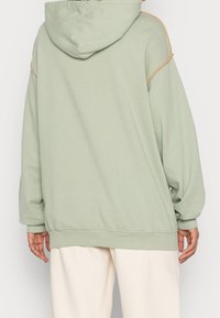 Sudadera verde claro con una gran capucha, puños y dobladillo acanalados. Presenta acentos de costura beige en contraste en los hombros. Textura de tela suave.