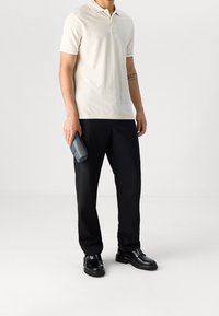 Krémové polo tričko s krátkými rukávy, černé zúžené kalhoty a černé kožené boty. Drží tmavě modrou kabelku. Minimalistický design.