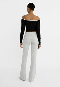 Zwarte, geribbelde, off-the-shoulder cropped top gecombineerd met lichtgrijze, strakkere flared broek. De outfit heeft een contrasterend detail bij de halslijn.