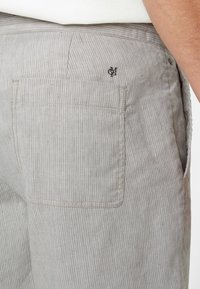 Grau gestreifte Hose mit einer Gesäßtasche, die über dezente Nähte und ein kleines Logo verfügt. Der Stoff hat ein strukturiertes, leichtes Erscheinungsbild.