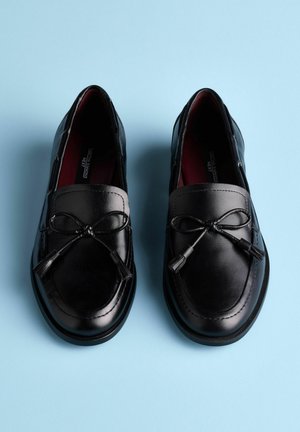 Černé kožené mokasíny s hladkou texturou, zdobené mašlí a třásněmi na přední části, navržené s kulatým tvarem.