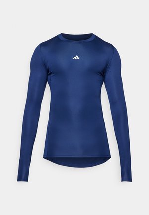 Marineblå langermet treningsskjorte; glatt, stretch stoff; rund hals; har en liten hvit logo på brystet; tettsittende design.