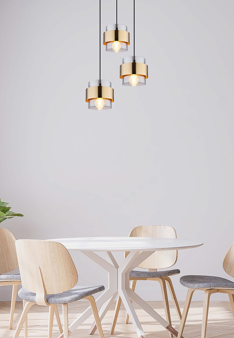 Drei Pendelleuchten mit goldenen und klaren Glaselementen hängen über einem weißen runden Tisch, der von hellen Holzstühlen mit grauen Kissen umgeben ist.